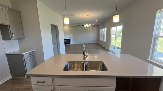 kitchen featuring sink, gray cabinetry, an island with sink, a notable chandelier, and pendant lighting