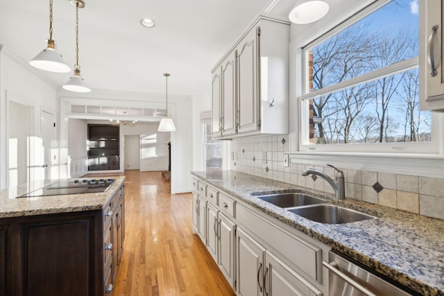 kitchen featuring hanging light fixtures, dishwasher, sink, and light stone counters