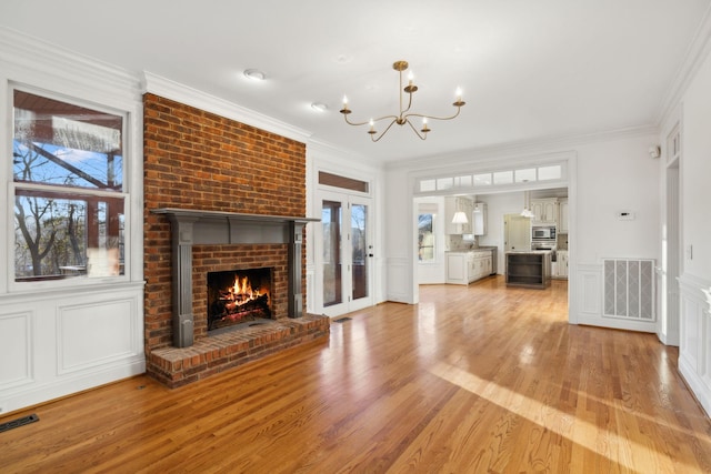 unfurnished living room with crown molding, a chandelier, a brick fireplace, and light wood-type flooring