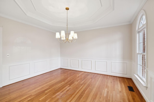 empty room with crown molding, a notable chandelier, a tray ceiling, and plenty of natural light