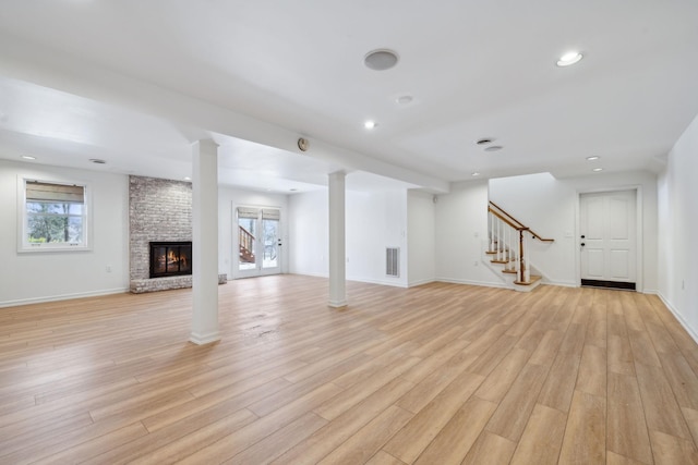 unfurnished living room featuring a brick fireplace, ornate columns, and light wood-type flooring