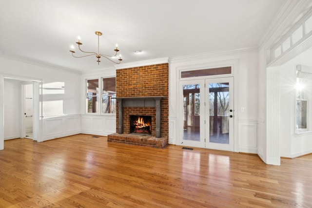 unfurnished living room featuring crown molding, a brick fireplace, an inviting chandelier, and light hardwood / wood-style floors