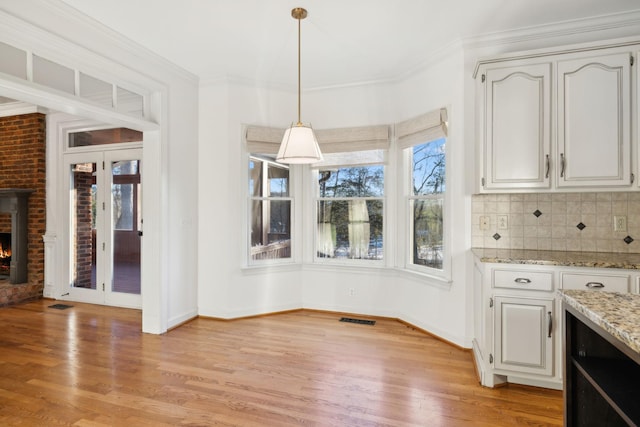 unfurnished dining area with a brick fireplace, ornamental molding, french doors, and light wood-type flooring