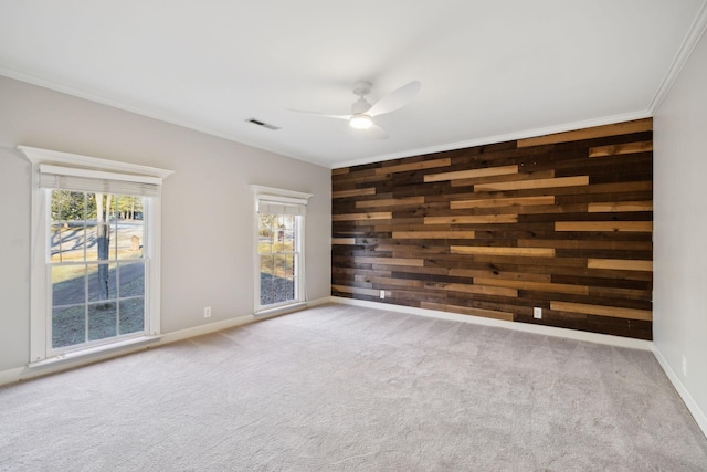 carpeted spare room with ornamental molding, a healthy amount of sunlight, ceiling fan, and wooden walls