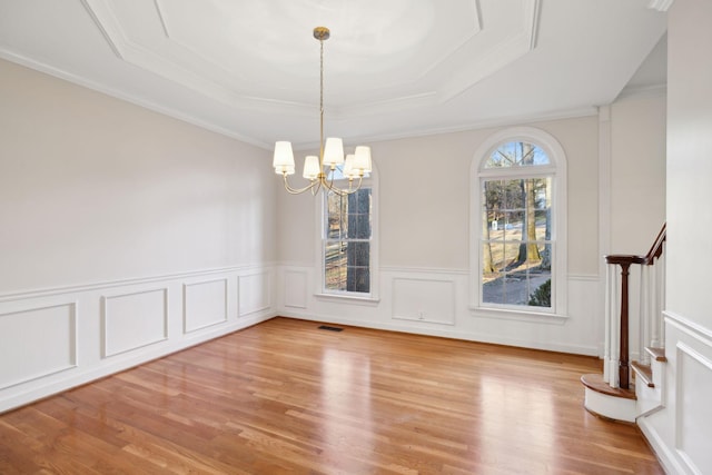 unfurnished dining area with a tray ceiling, light hardwood / wood-style flooring, ornamental molding, and a chandelier