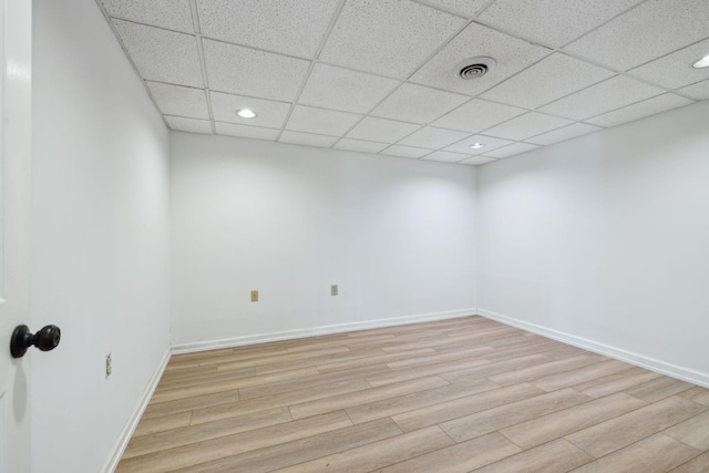 spare room with a paneled ceiling and light wood-type flooring