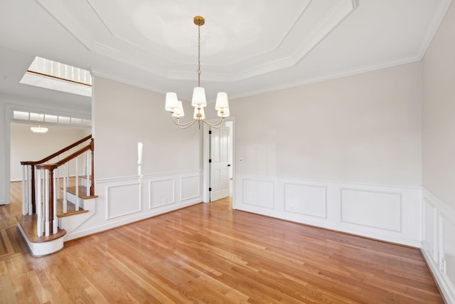 unfurnished dining area with ornamental molding, light hardwood / wood-style flooring, a chandelier, and a tray ceiling