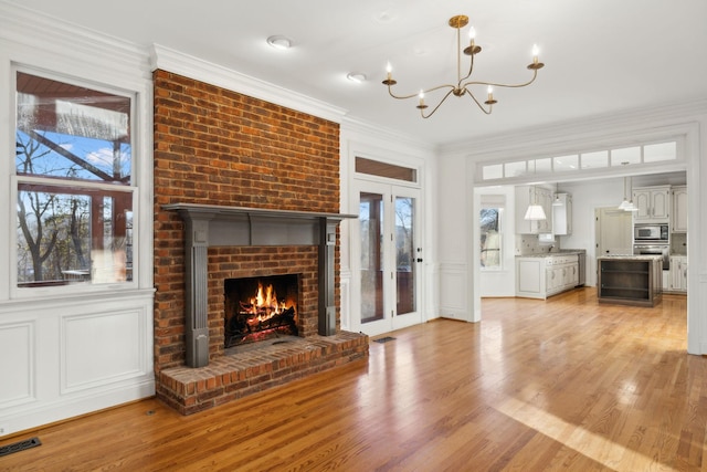 unfurnished living room with ornamental molding, a chandelier, light hardwood / wood-style floors, and a brick fireplace