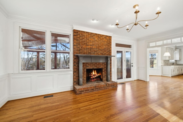 unfurnished living room with crown molding, a brick fireplace, a notable chandelier, and light hardwood / wood-style floors