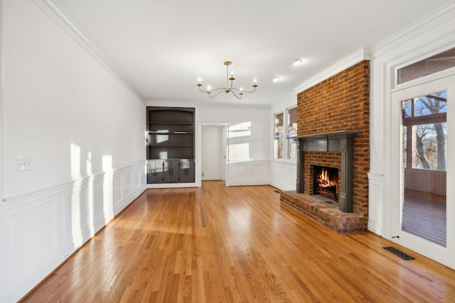 unfurnished living room with crown molding, a fireplace, light wood-type flooring, and a notable chandelier