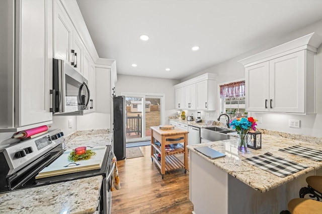 kitchen with a kitchen bar, white cabinetry, hardwood / wood-style flooring, stainless steel appliances, and light stone countertops