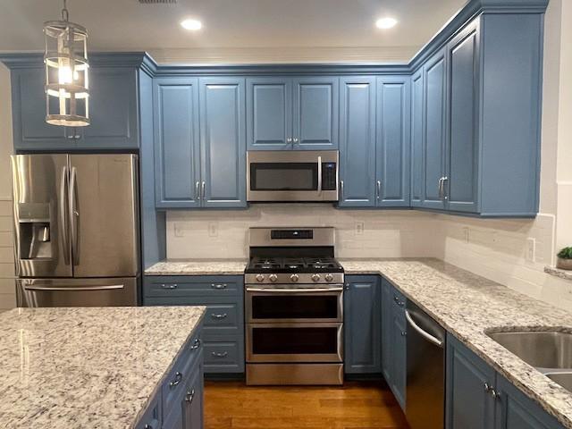 kitchen featuring pendant lighting, blue cabinetry, appliances with stainless steel finishes, dark hardwood / wood-style floors, and decorative backsplash