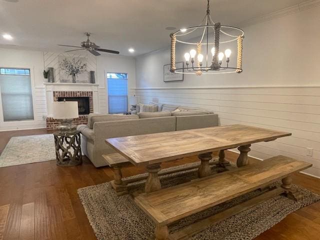 dining area featuring crown molding, dark hardwood / wood-style flooring, ceiling fan with notable chandelier, and a brick fireplace