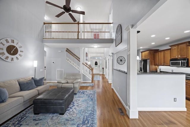 living room with ceiling fan, a towering ceiling, light hardwood / wood-style flooring, and ornate columns