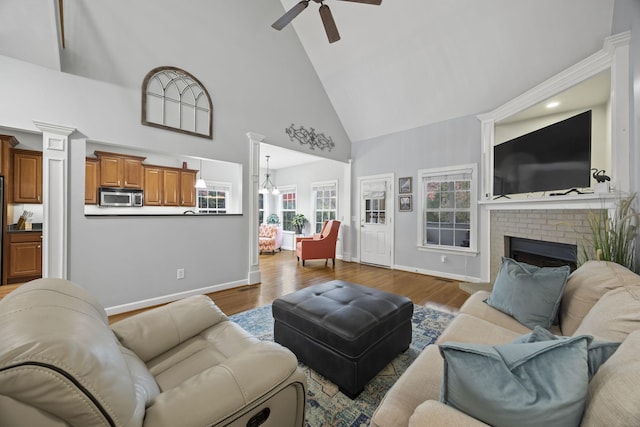 living room with a brick fireplace, high vaulted ceiling, hardwood / wood-style floors, and ornate columns