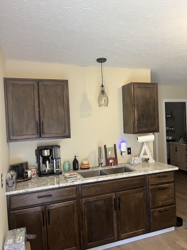 kitchen featuring light stone counters, sink, dark brown cabinets, and light hardwood / wood-style flooring