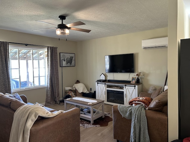 living room with a wall mounted air conditioner, a textured ceiling, light hardwood / wood-style floors, and ceiling fan