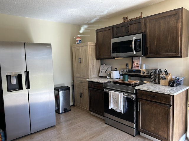 kitchen with dark brown cabinets, light wood-type flooring, a textured ceiling, and appliances with stainless steel finishes