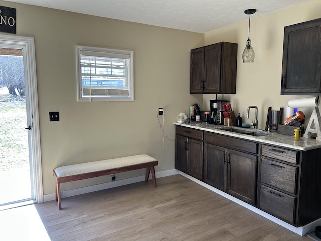 kitchen with dark brown cabinetry, sink, light hardwood / wood-style floors, and hanging light fixtures