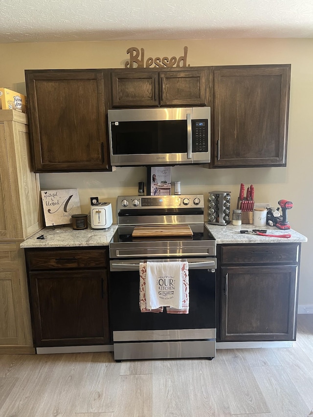 kitchen with appliances with stainless steel finishes, dark brown cabinets, and light hardwood / wood-style flooring