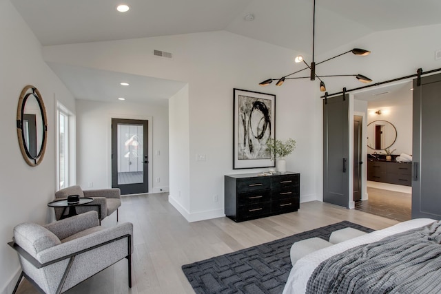 bedroom featuring a barn door, connected bathroom, lofted ceiling, and light hardwood / wood-style floors