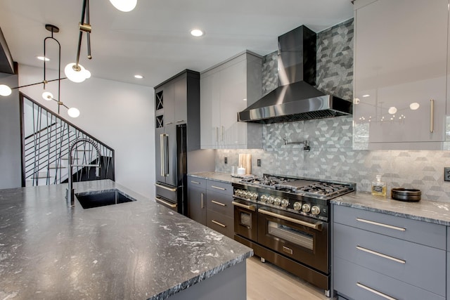 kitchen featuring pendant lighting, sink, high quality appliances, dark stone counters, and wall chimney exhaust hood