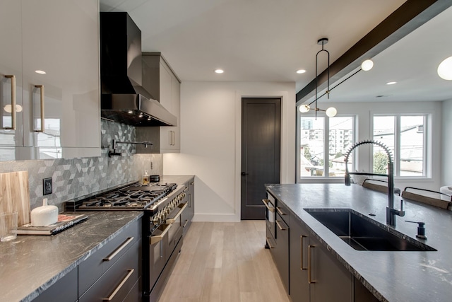 kitchen featuring wall chimney exhaust hood, sink, double oven range, pendant lighting, and light hardwood / wood-style floors