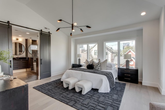 bedroom featuring ensuite bath, vaulted ceiling, light hardwood / wood-style floors, and a barn door