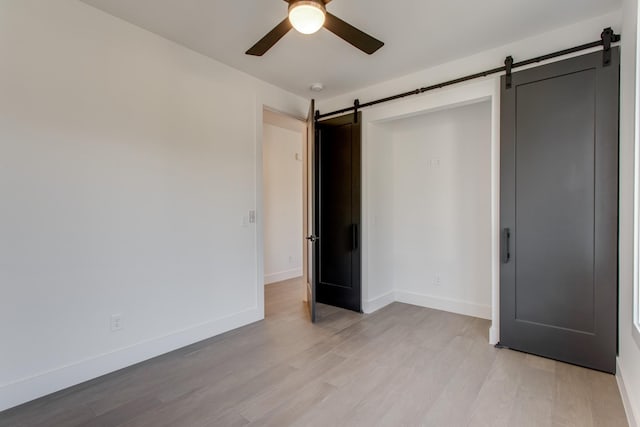 unfurnished bedroom featuring a barn door, light wood-type flooring, and ceiling fan