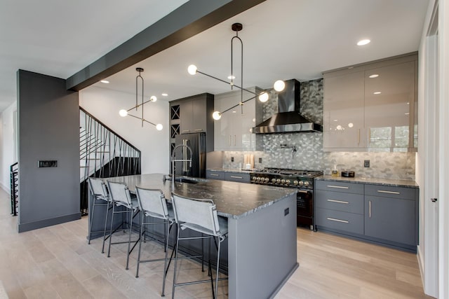 kitchen with a center island with sink, high end appliances, pendant lighting, and wall chimney range hood