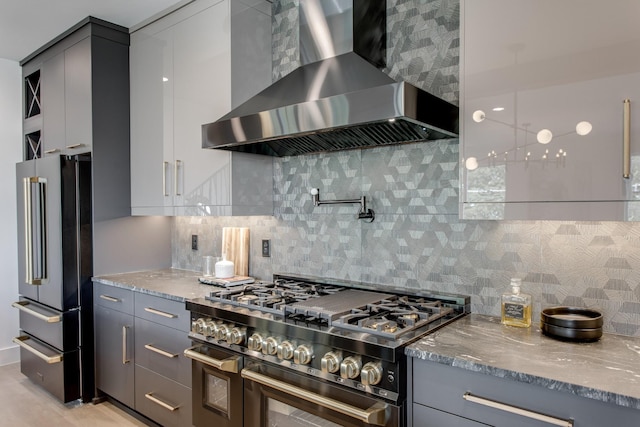 kitchen featuring gray cabinets, decorative backsplash, high end appliances, light stone counters, and wall chimney range hood