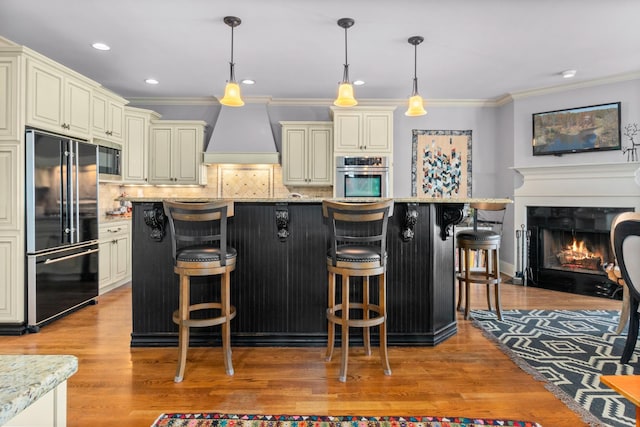 kitchen featuring a breakfast bar area, stainless steel oven, high quality fridge, custom range hood, and cream cabinetry