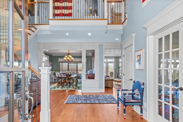 entrance foyer featuring hardwood / wood-style flooring, a towering ceiling, ornamental molding, and a notable chandelier