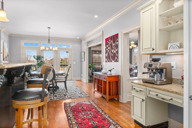 kitchen featuring pendant lighting, crown molding, an inviting chandelier, light stone counters, and light wood-type flooring