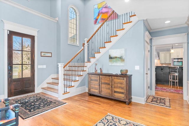 foyer featuring crown molding, light hardwood / wood-style flooring, and a high ceiling