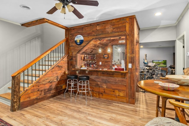 bar featuring ceiling fan, ornamental molding, wood walls, and light wood-type flooring