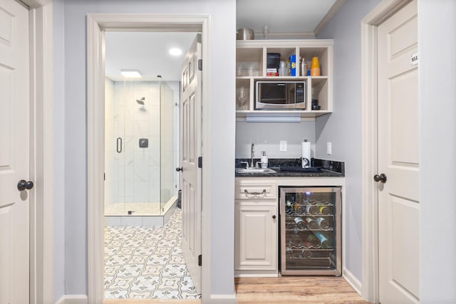 bar featuring sink, stainless steel microwave, beverage cooler, dark stone counters, and light wood-type flooring