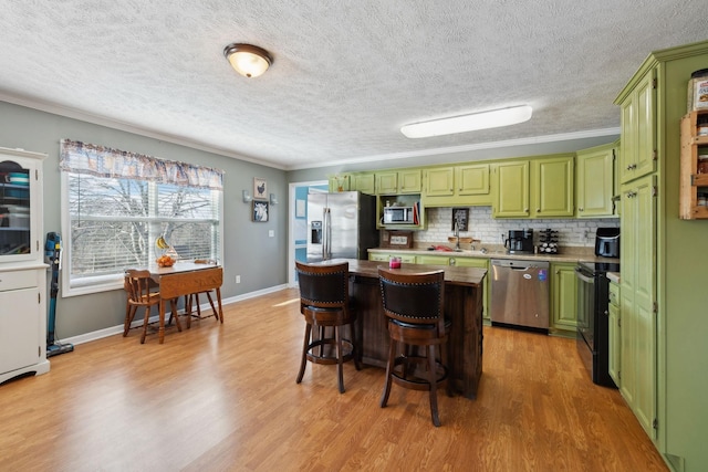 kitchen with a breakfast bar, sink, green cabinetry, stainless steel appliances, and decorative backsplash