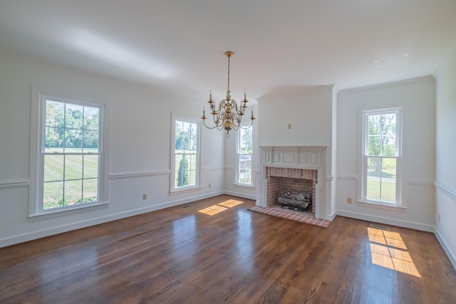 unfurnished living room featuring crown molding, dark hardwood / wood-style flooring, a chandelier, and a brick fireplace