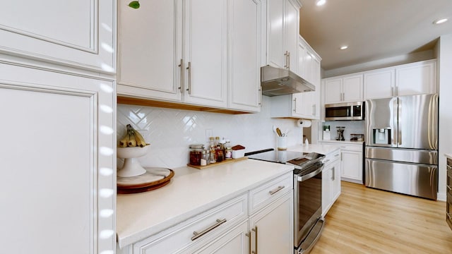 kitchen with under cabinet range hood, stainless steel appliances, white cabinetry, light countertops, and light wood-type flooring