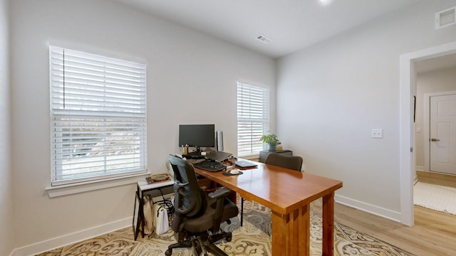 office area with plenty of natural light, visible vents, light wood-style flooring, and baseboards