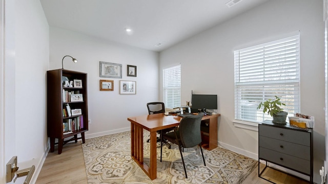 office space with light wood-style floors, visible vents, and baseboards