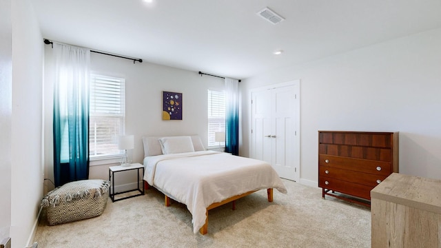 bedroom featuring multiple windows, a closet, visible vents, and light colored carpet