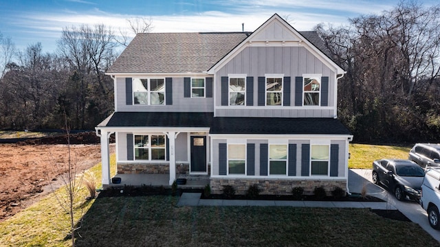 craftsman inspired home featuring stone siding, a shingled roof, board and batten siding, and a front yard