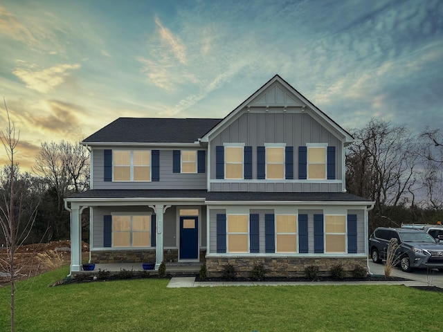 craftsman-style house with stone siding, a porch, board and batten siding, and a yard