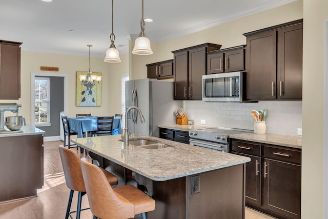 kitchen featuring dark brown cabinets, stainless steel appliances, an island with sink, and hanging light fixtures