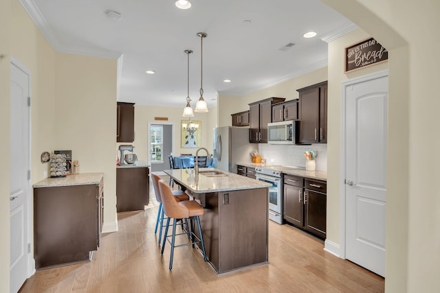 kitchen with pendant lighting, stainless steel appliances, crown molding, and light stone countertops