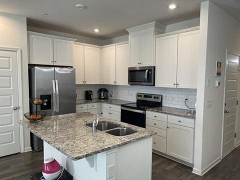 kitchen featuring light stone countertops, white cabinetry, appliances with stainless steel finishes, and a kitchen island with sink