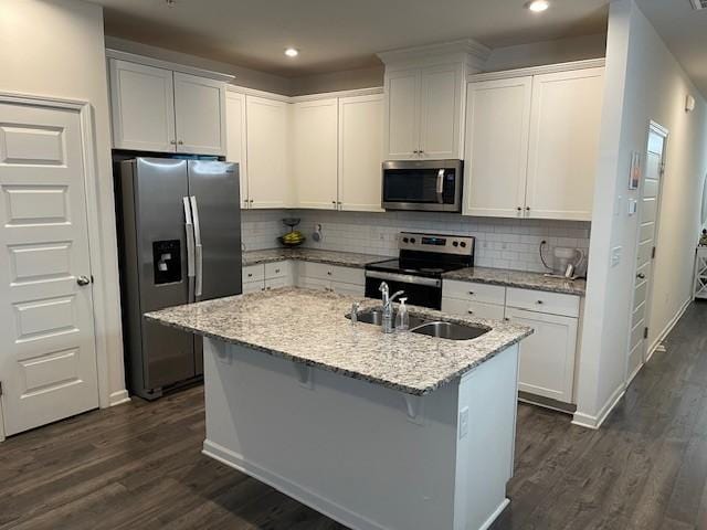 kitchen with white cabinets, light stone counters, stainless steel appliances, and an island with sink