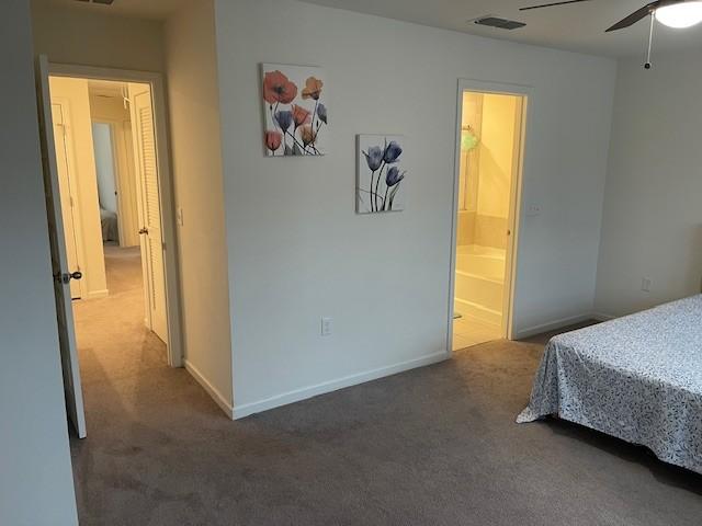 bedroom with dark colored carpet, visible vents, ceiling fan, ensuite bath, and baseboards